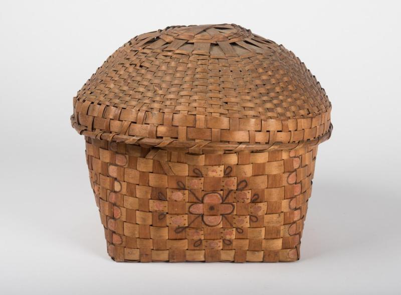 Lidded brown basket woven with strips of ash wood and decorated with a simple floral and dot design on the side.