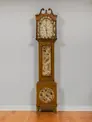 Tall grandfather-style clock in a wooden case painted to resemble different types of wood grains. 