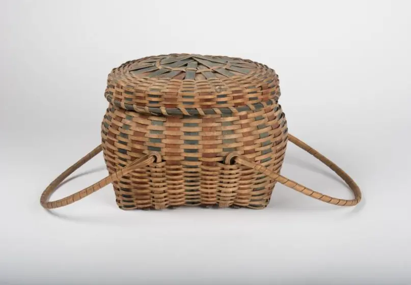 Oval-shaped woven basket with lid and movable handles, with indigo and red splints interwoven throughout.