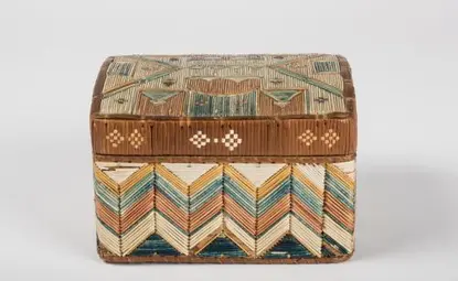 A small colorful box with a lid is decorated with lengths of porcupine quills forming a geometric design on the lid and chevron patterns on sides.
